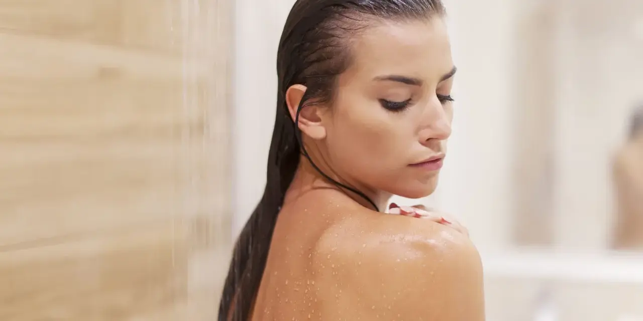 Mujer en la ducha, con gotas de agua en su piel. Pregúntate cada cuanto exfoliar el cuerpo para una piel radiante.