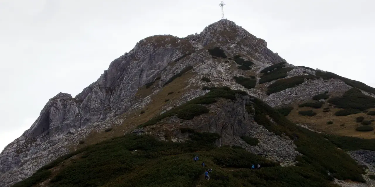 Wspinaczka na Giewont. Grupa turystów pokonuje skaliste zbocze, gdzie w trudniejszych miejscach pomagają łańcuchy.