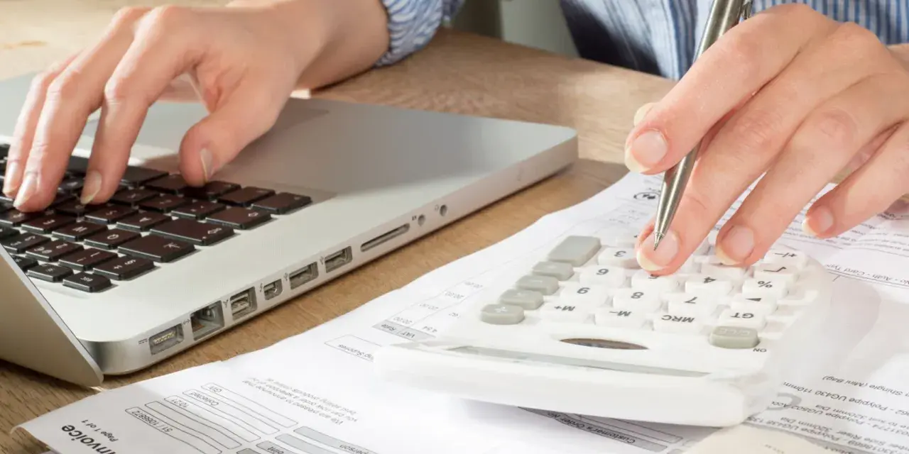 Main tenant calcule son solde de tout compte imposable sur une calculatrice, un ordinateur et des factures.