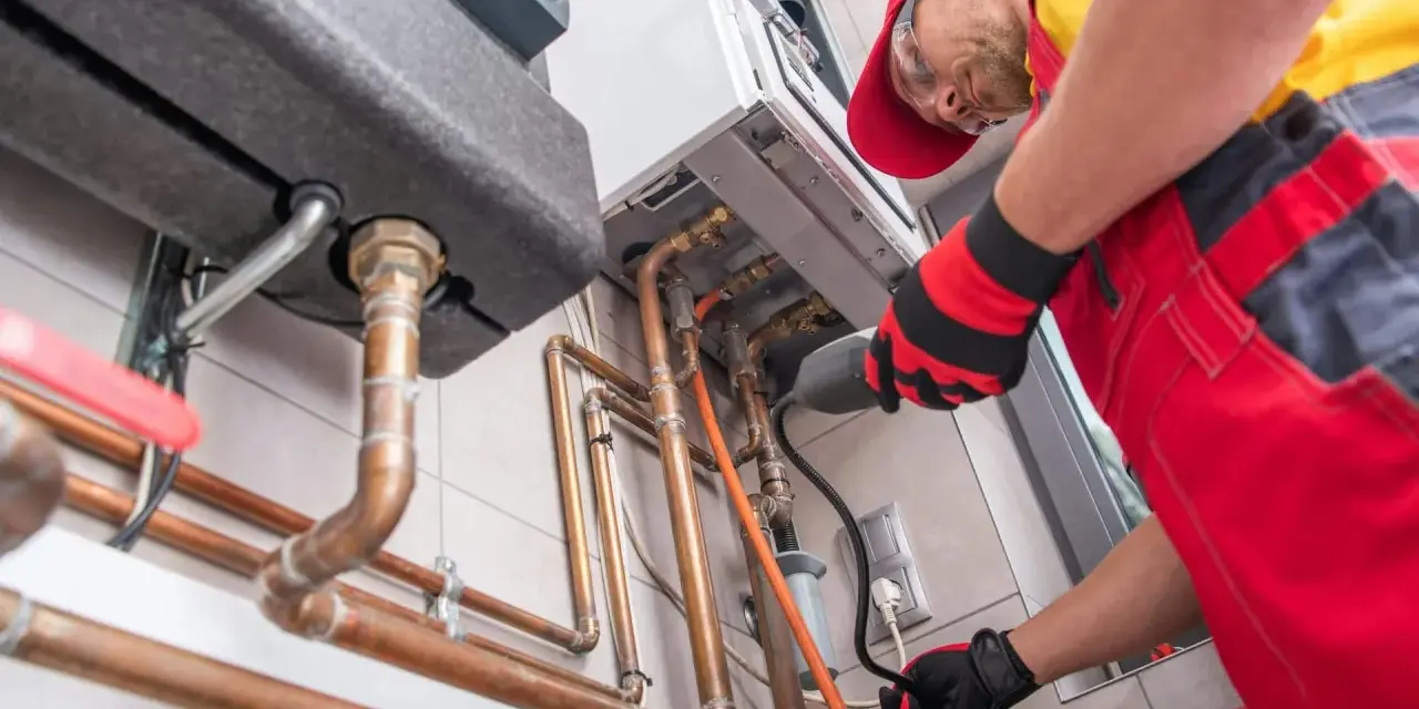Un technicien installe une chaudière à gaz, une étape clé pour ma prime rénov. Il manipule des tuyaux en cuivre avec soin.