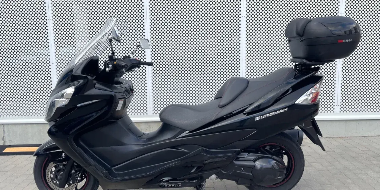 Czarny skuter Suzuki Burgman 400 z kufrem SH46 na tle perforowanej białej ściany.