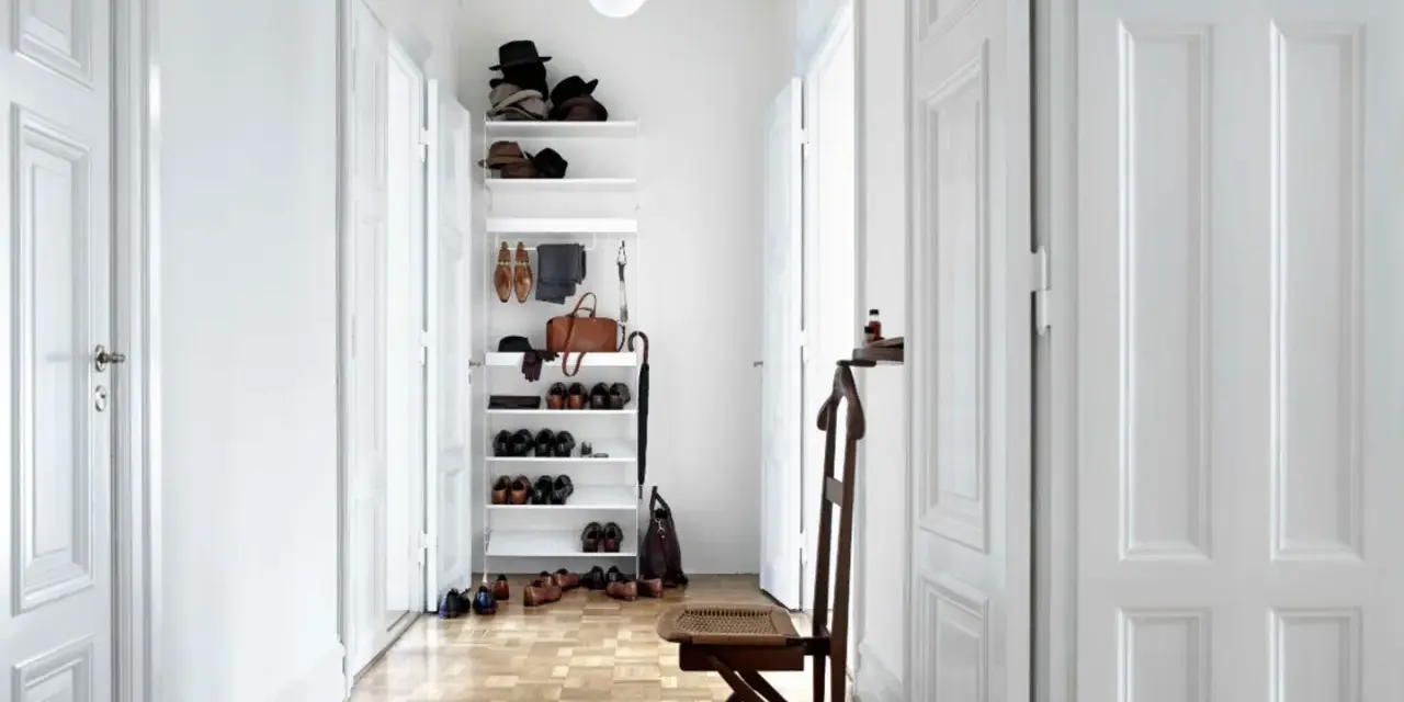 Ein heller, schmaler Flur wirkt optisch breiter durch weiße Türen und eine offene Regalwand mit Schuhen und Accessoires.