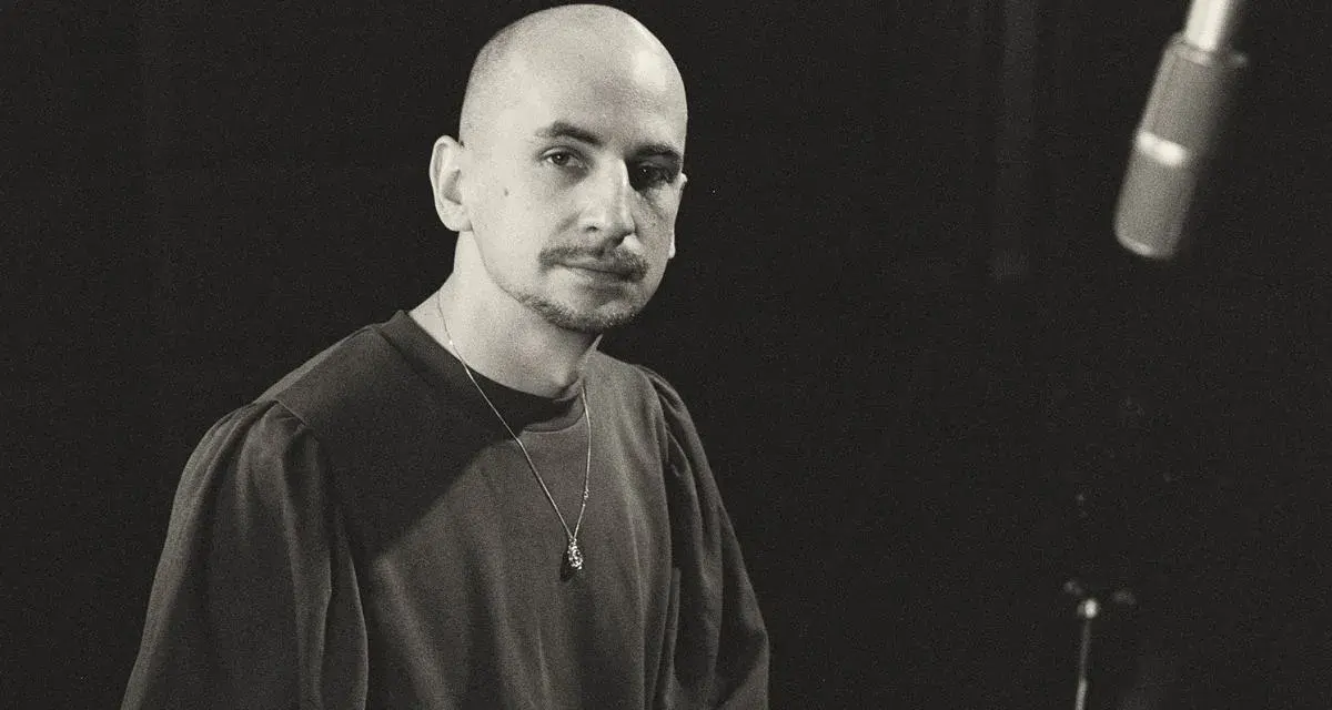 Marek Pędziwiatr, z charakterystyczną łysą głową i wąsikiem, w ciemnej bluzie i z naszyjnikiem, przygotowuje się do nagrania.