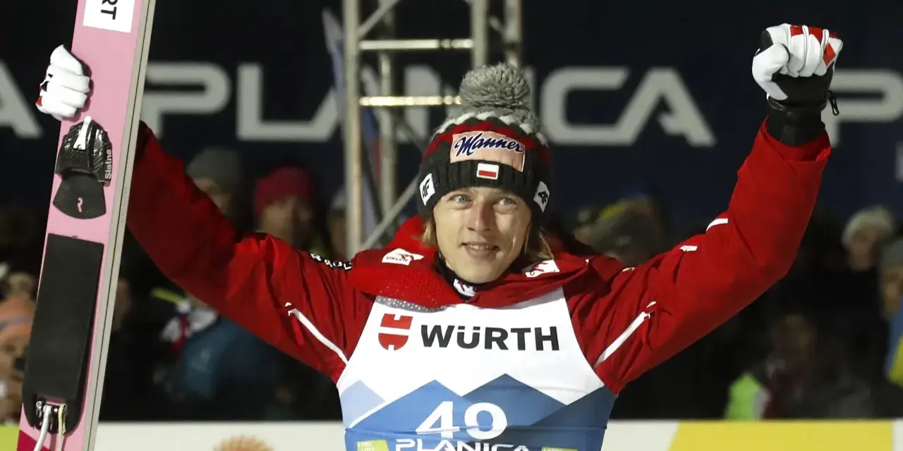 Skoczek narciarski w czerwonej kurtce i czapce z polską flagą świętuje zwycięstwo na skoczni. Mistrzostwa świata w skokach narciarskich.
