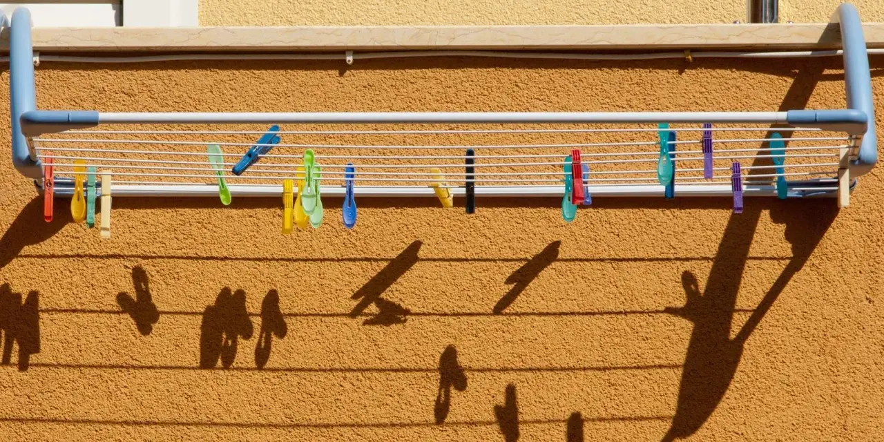 Variados tipos de tendederos exteriores con pinzas de colores sujetan la ropa. Las sombras proyectadas crean un patrón interesante sobre la pared texturizada.