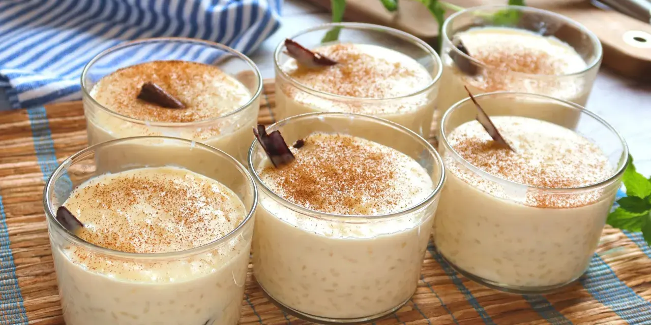 Seis vasitos de cremoso arroz con leche, espolvoreados con canela y decorados con una ramita de canela.