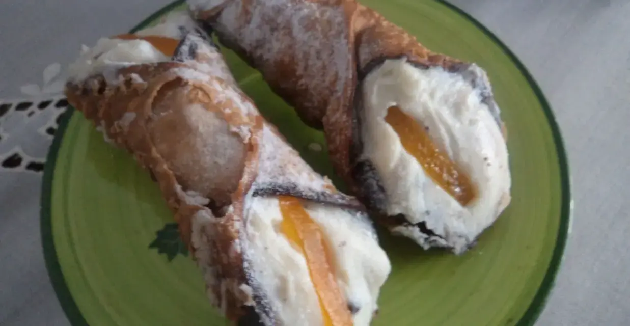 Dwa pyszne cannoli z kremem i kandyzowaną skórką pomarańczową, posypane cukrem pudrem. Ten makaron to prawdziwa rozkosz!