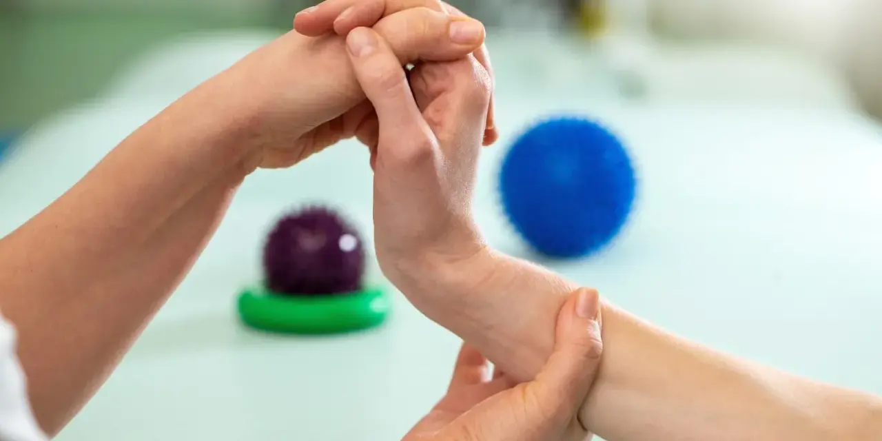 Fizjoterapeuta pomaga pacjentowi w ćwiczeniach na palec trzaskający, używając masażu i piłeczek do rehabilitacji.