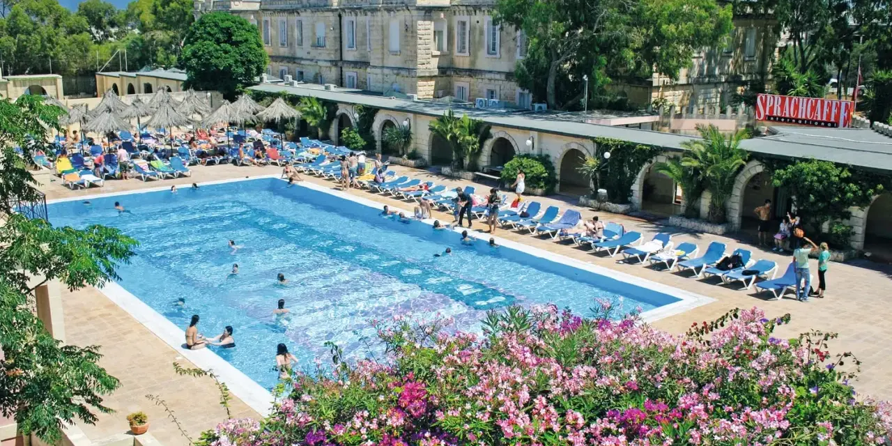 Profitez de vos vacances scolaires à Malte au bord de cette piscine animée, entourée de transats et de végétation luxuriante.