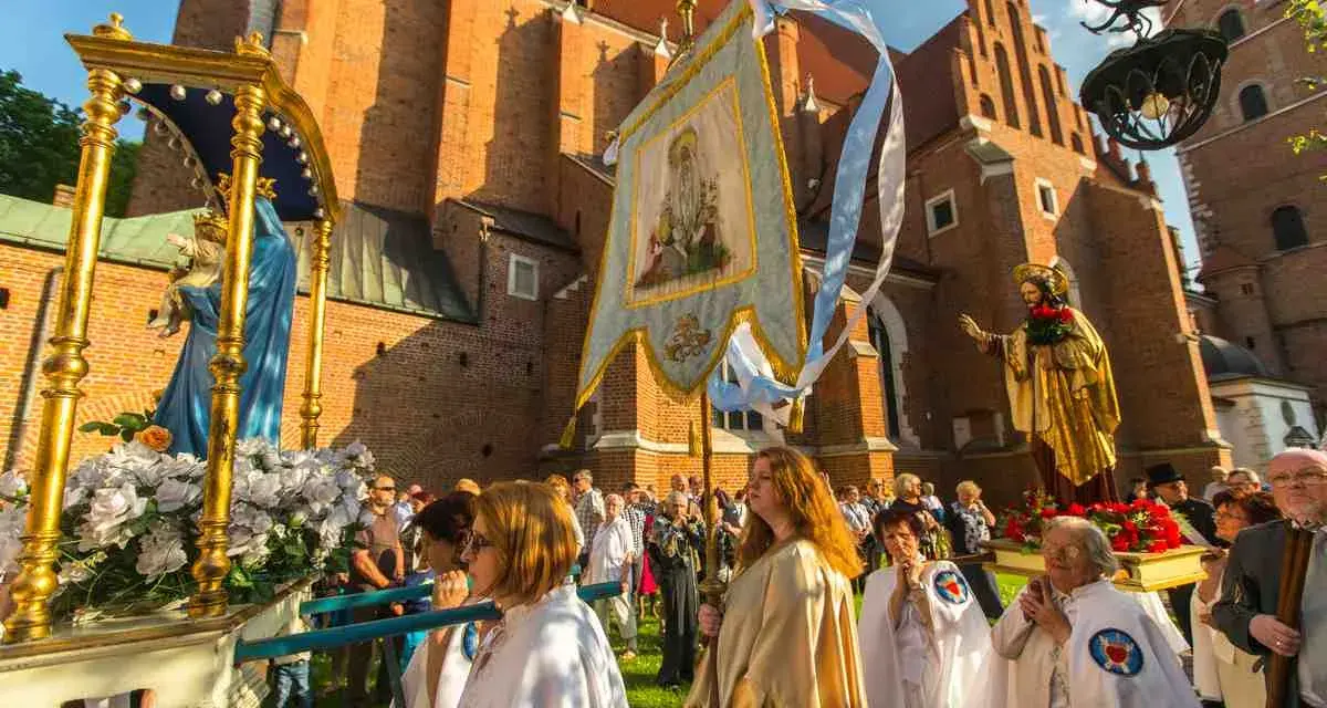 Prozession mit Marienstatue und Fahne vor einer Kirche. Menschen in weißen Gewändern, ein Festtag in Polen.