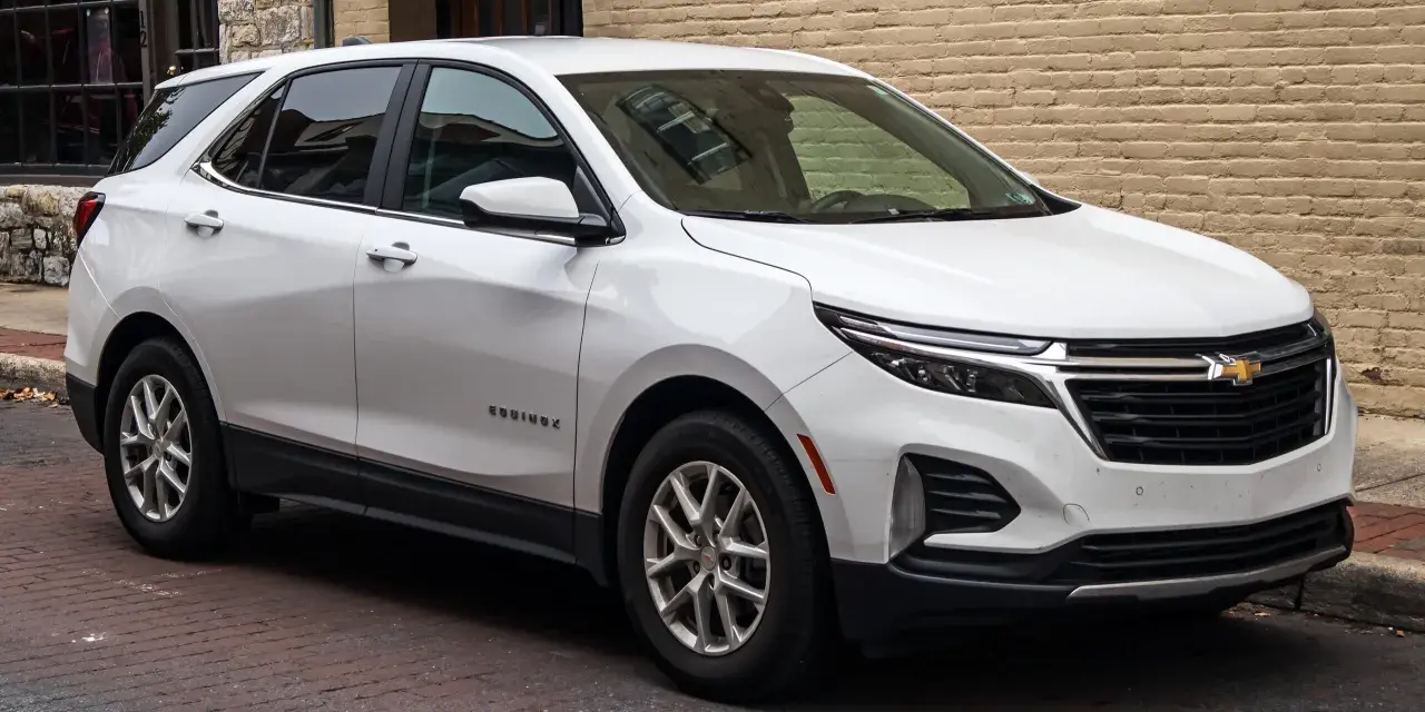 Biały Chevrolet Equinox stoi zaparkowany na brukowanej ulicy, obok ceglanego budynku.