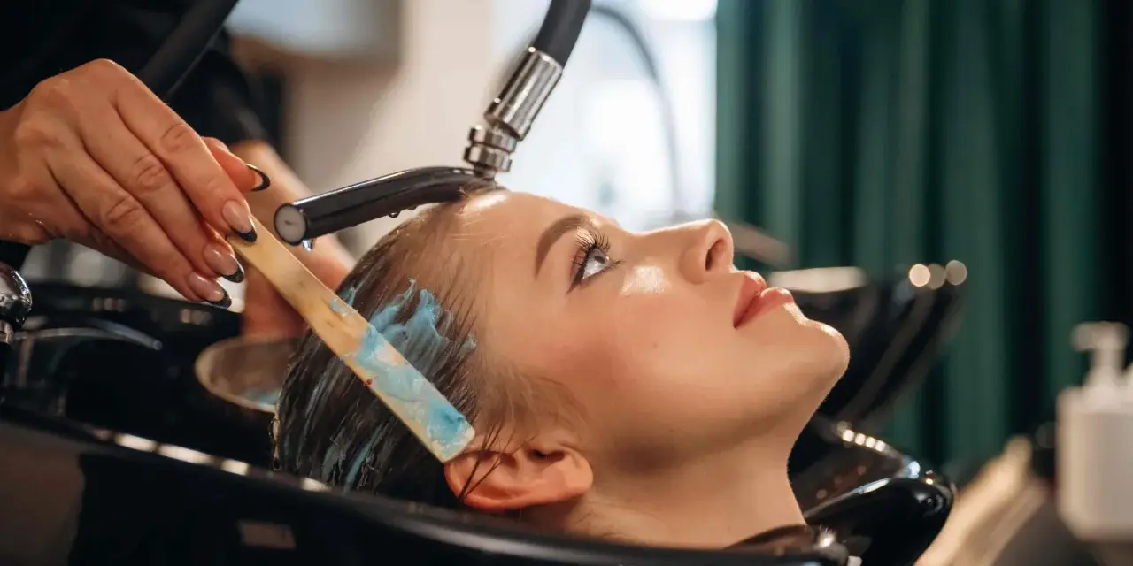 Profesjonalna pielęgnacja włosów farbowanych w salonie. Stylistka nakłada maskę na mokre włosy klientki.