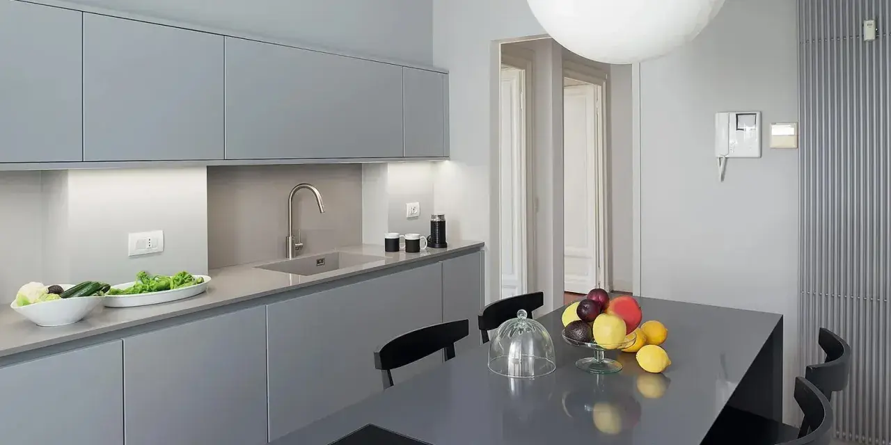 Cucina moderna con pensili e basi grigie. Il colore pareti neutro esalta la pulizia delle linee. Tavolo con frutta fresca.