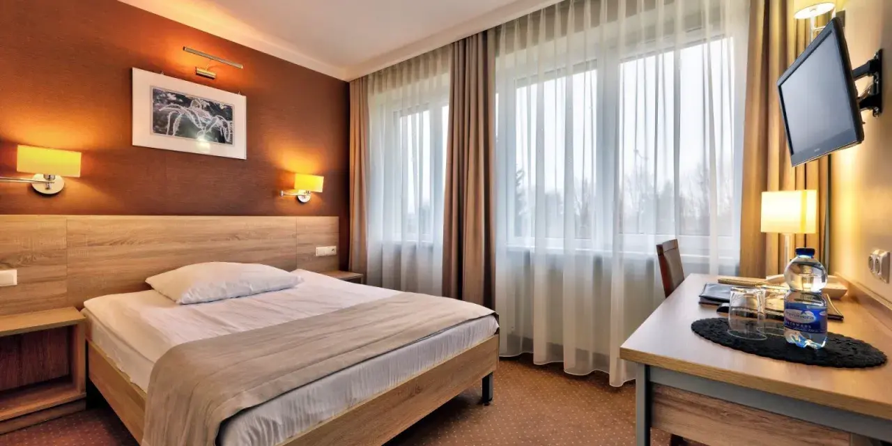 Przytulny pokój hotelowy w Białymstoku z wygodnym łóżkiem, biurkiem i telewizorem.