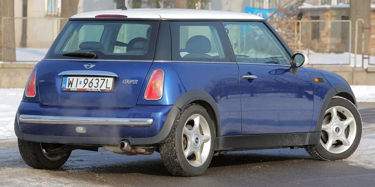 Niebieski Mini Cooper R50 z białym dachem, zaparkowany na zaśnieżonej drodze.