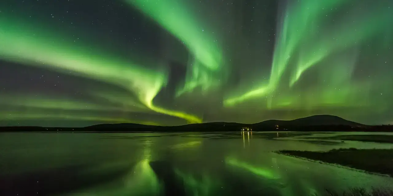 Grönt norrsken dansar över en frusen sjö i Finland. Stjärnor lyser på himlen och speglar sig i vattnet.