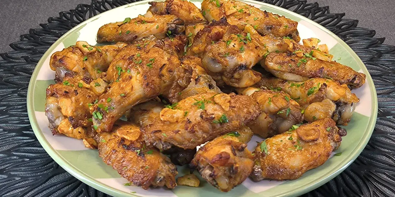 Alitas de pollo doradas con ajo y perejil en un plato verde.