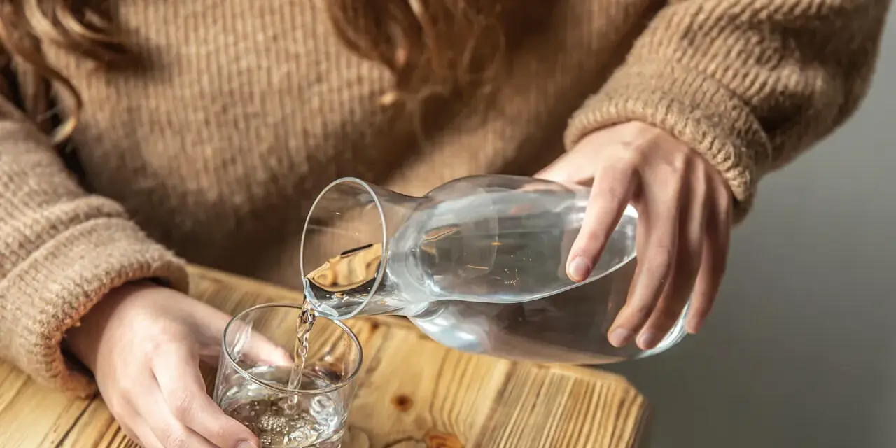 Dłonie nalewają wodę z karafki do szklanki. Pamiętaj, by stay hydrated.