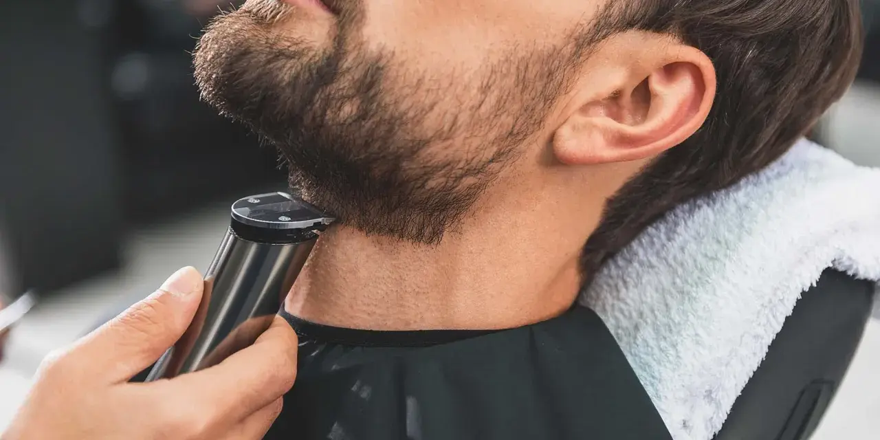 Barbero perfilando barba con recortadora, creando diseños de barba modernos.