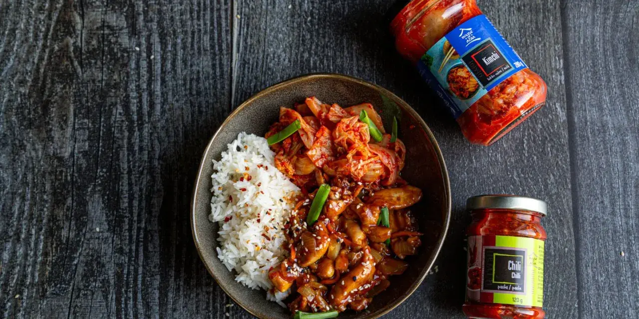 Miseczka z ryżem i kurczakiem po koreańsku, z dodatkiem kimchi i sosu chili.