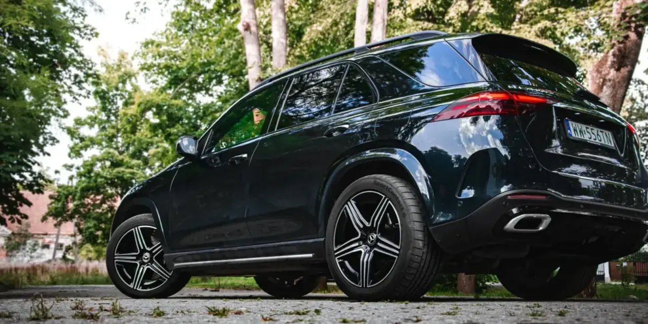 Ciemny Mercedes GLE 350 zaparkowany na kamienistej drodze, otoczony zielenią drzew.