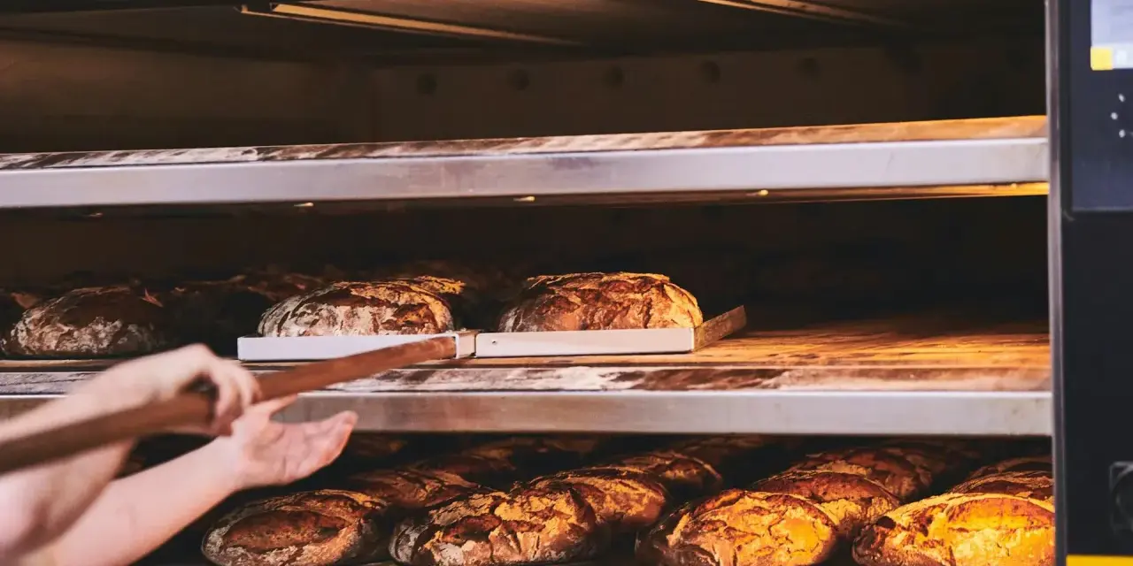 Bäcker lässt den **backofen spalt offen lassen beim backen** für knuspriges Brot. Mehrere Brote auf Regalen im Ofen.