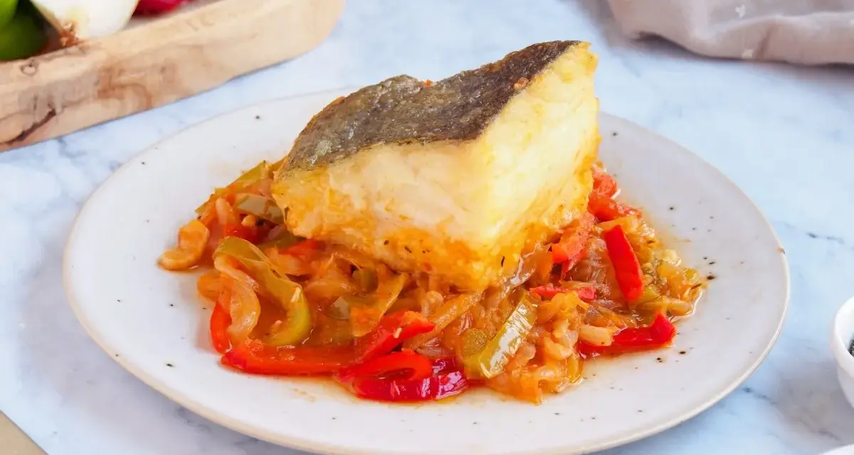 Un delicioso bacalao encebollado reposa sobre una cama de pimientos y cebolla.