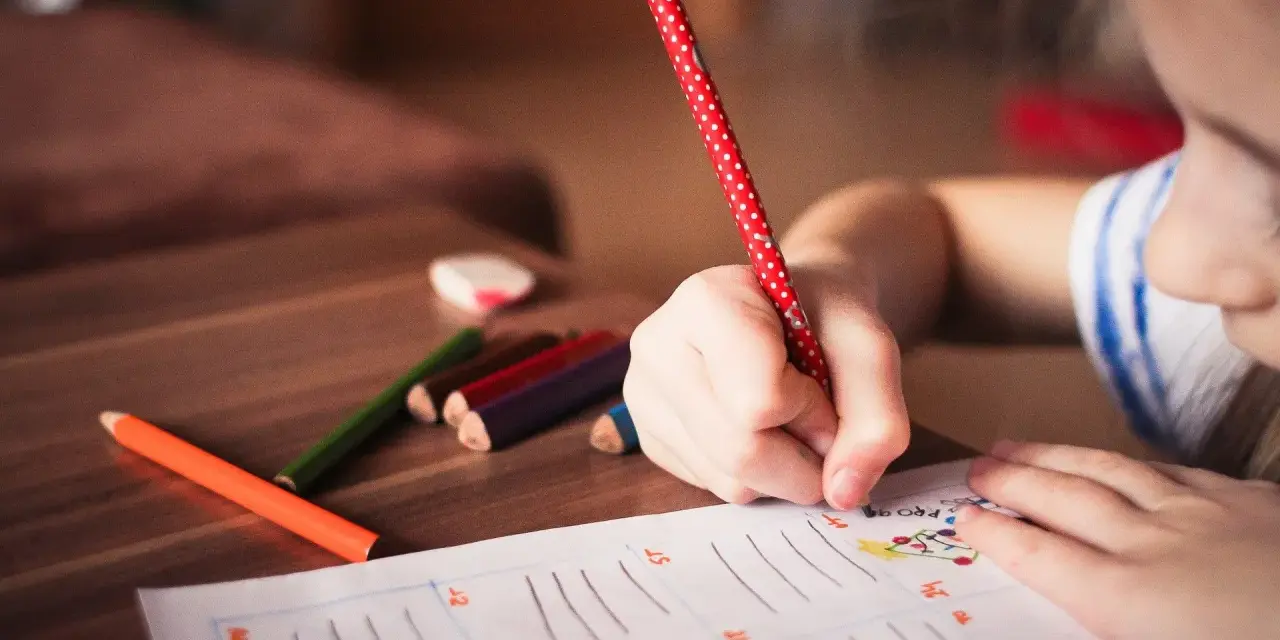 Dziecko zmagające się z dysleksją, dysgrafią, dysortografią i dyskalkulią pisze kredkami.