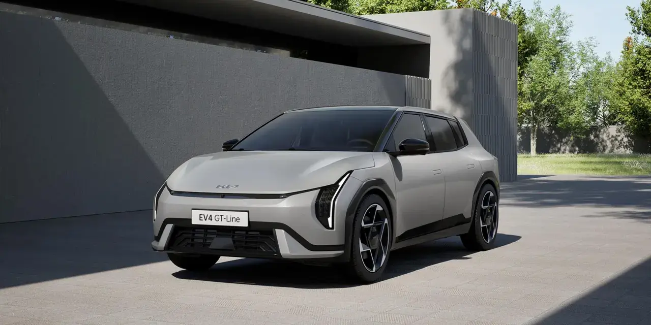 Nowoczesny, jasnoszary Kia EV4 GT-Line stoi na podjeździe przed minimalistycznym budynkiem.