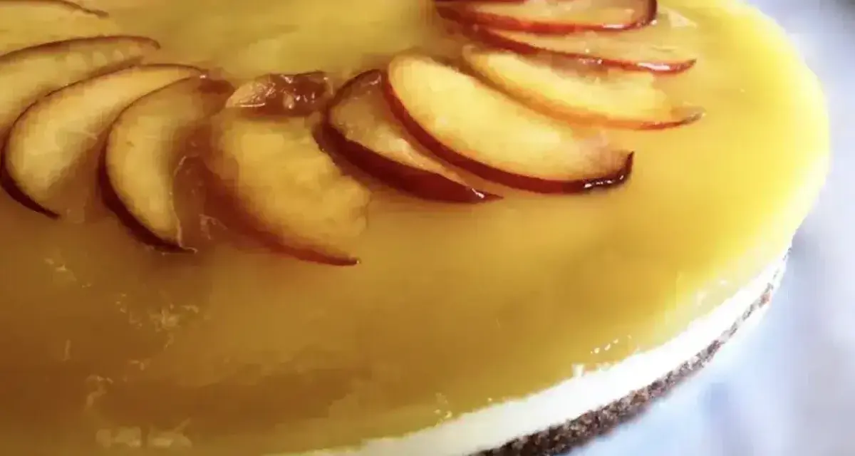 Cheesecake alla pesca con fette di pesca fresca disposte a raggiera sulla glassa gialla.