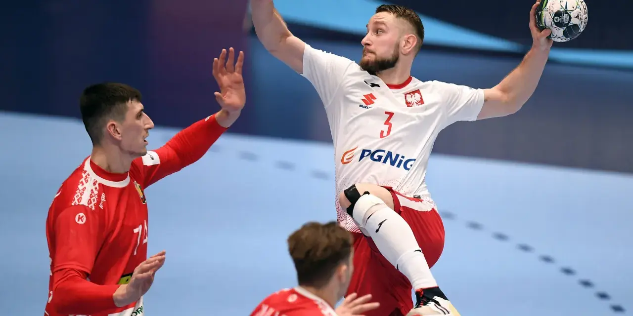 Gracz w piłkę ręczną w skoku, z piłką w dłoni, celuje do bramki. Jego przeciwnik próbuje go zatrzymać.