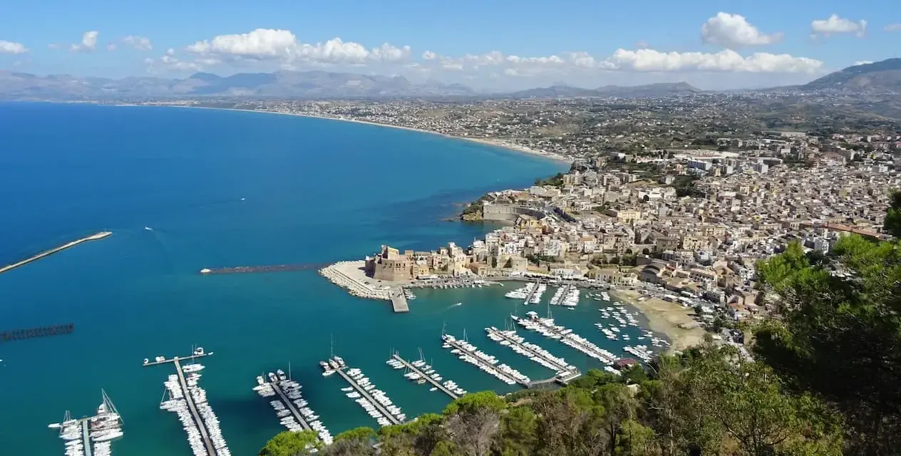 Vista panoramica di Castellammare del Golfo, con il castello, il porto turistico pieno di barche e la costa siciliana.