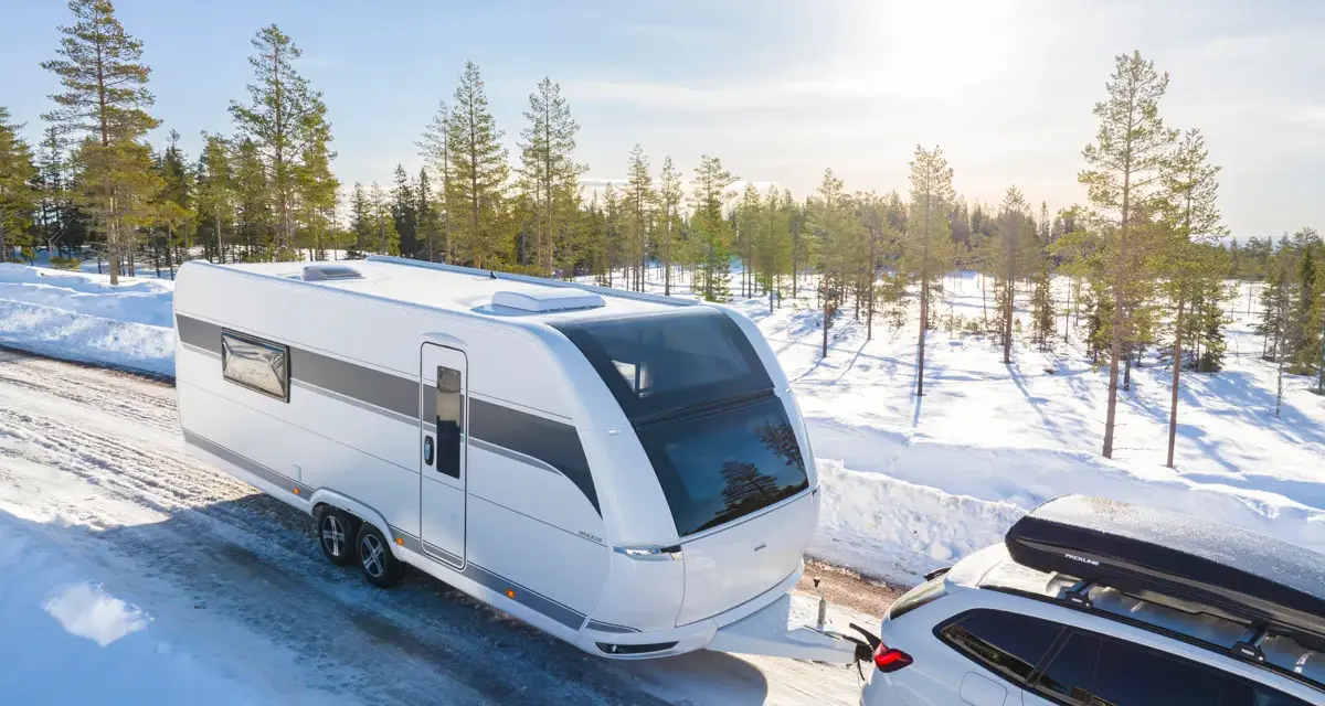 Vit husvagn dras av bil genom snöig skog. Den bästa husvagnen för äventyr nära Haparanda.
