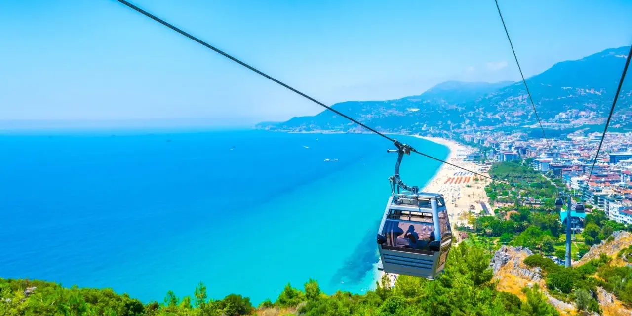 Kolejka linowa nad turkusowym morzem i plażą w Alanyi. Widok z góry na miasto i wybrzeże. Czy Alanya jest bezpieczna? Tak, wygląda na spokojną i piękną.