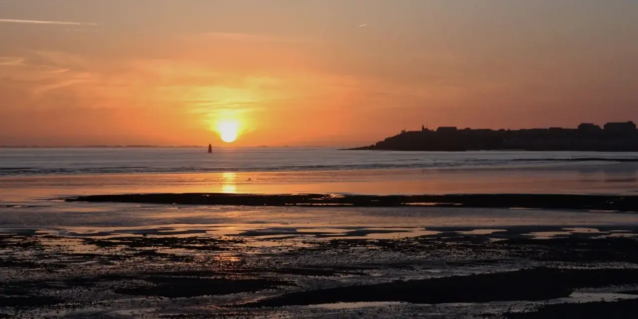 Coucher de soleil sur la mer à Saint-Pair-sur-Mer. La lumière dorée illumine le ciel et l'eau, invitant à la contemplation.