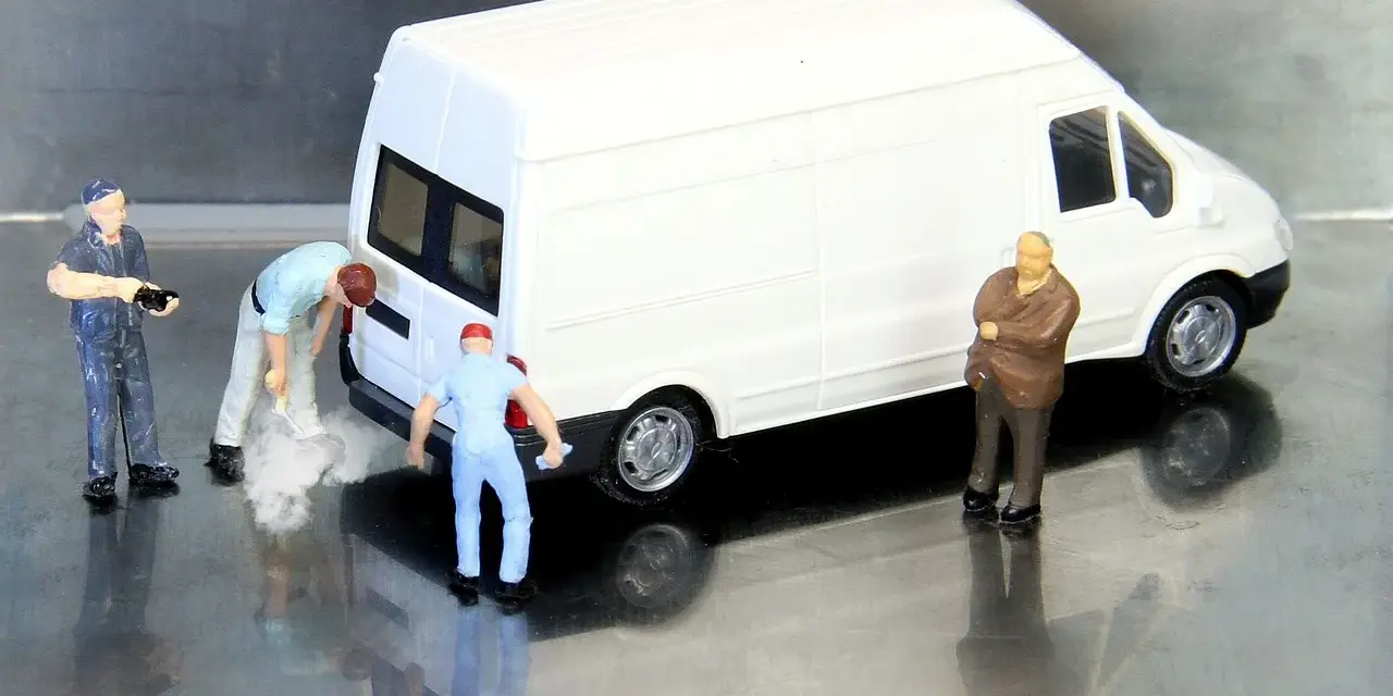 Miniaturowi pracownicy zajmują się białym busem budowlanym. Jeden z nich czyści tył pojazdu, inny trzyma narzędzie, a trzeci obserwuje.