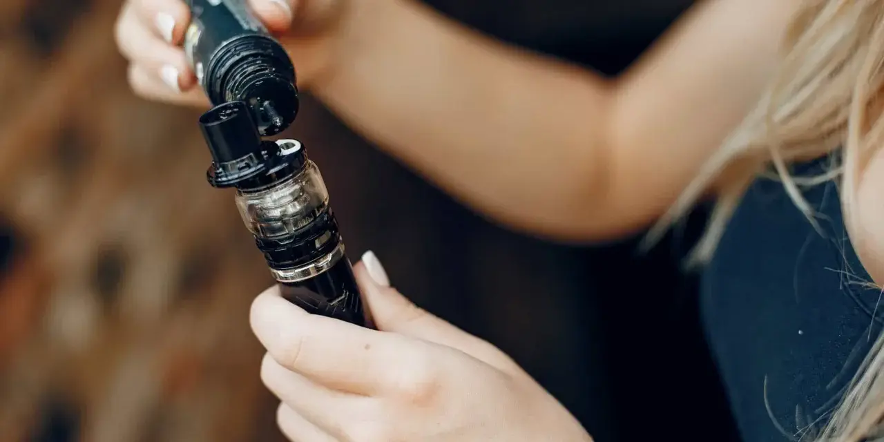 Manos rellenando un vaporizador con líquido de nicotina salina.