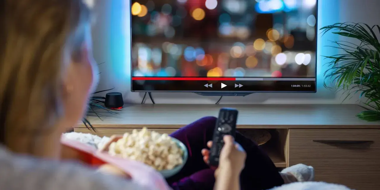 Persona relajada viendo una serie en francés en la televisión, con palomitas y mando a distancia.
