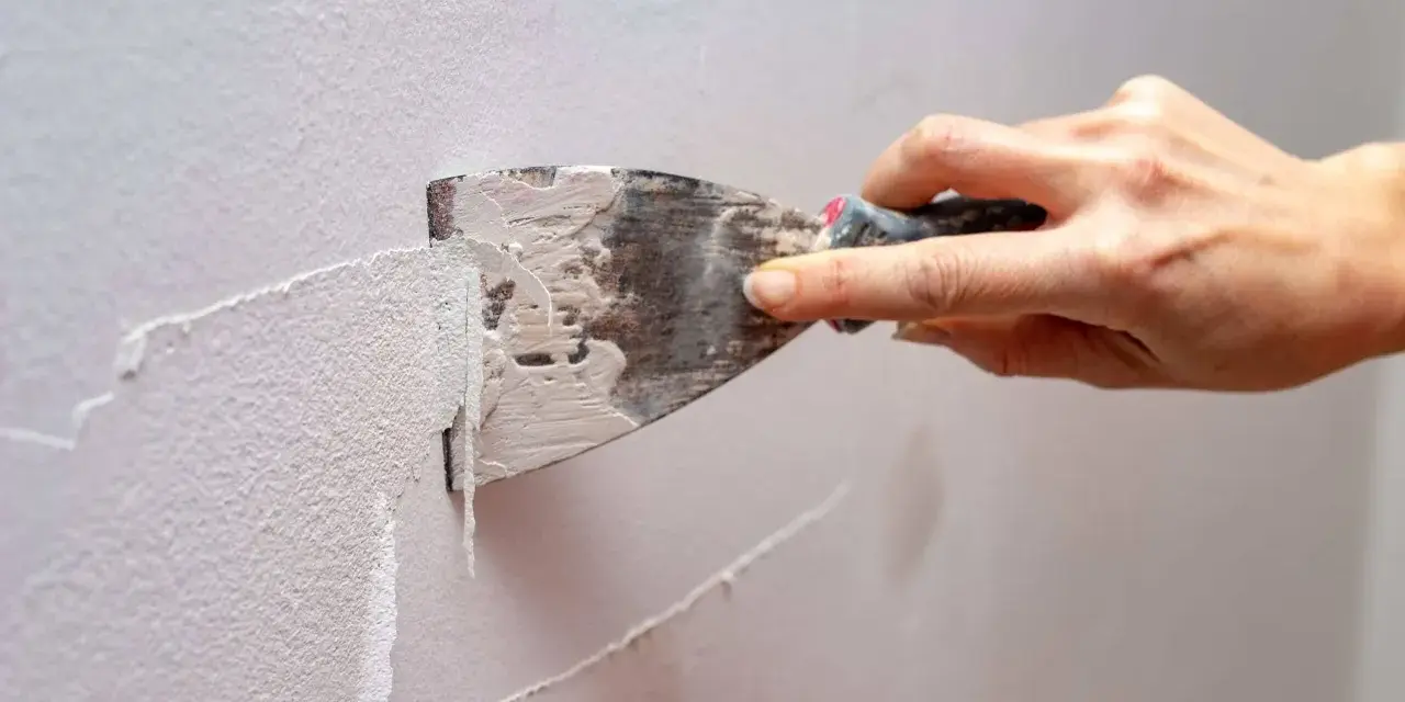 Mano usa una spatola per rimuovere la vecchia pittura, mostrando come grattare un muro per prepararlo.