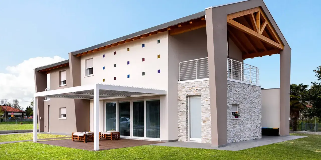 Casa moderna con tetto in legno a vista, facciata decorata con quadrati colorati e un portico bianco.