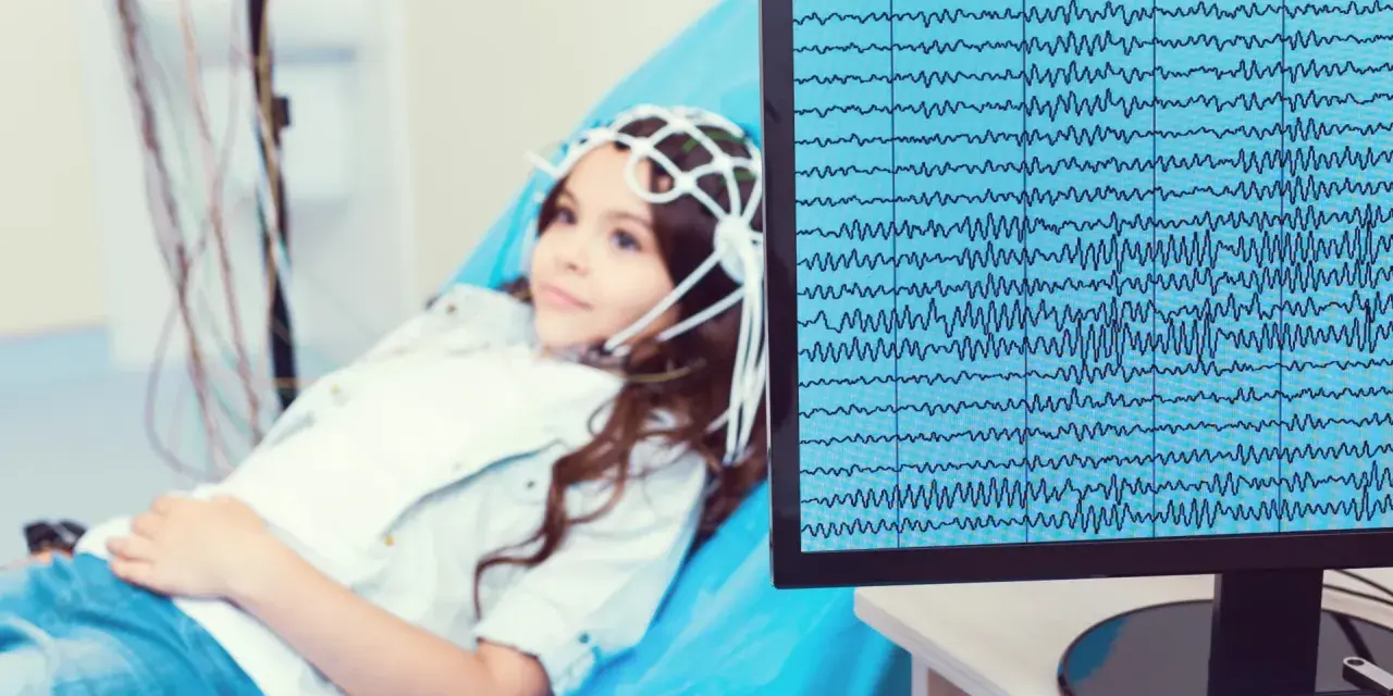 Dziewczynka z czepkiem EEG leży na kozetce, a na monitorze widać zapis fal mózgowych. Badanie pomaga zrozumieć zespół Aspergera a wynik EEG.