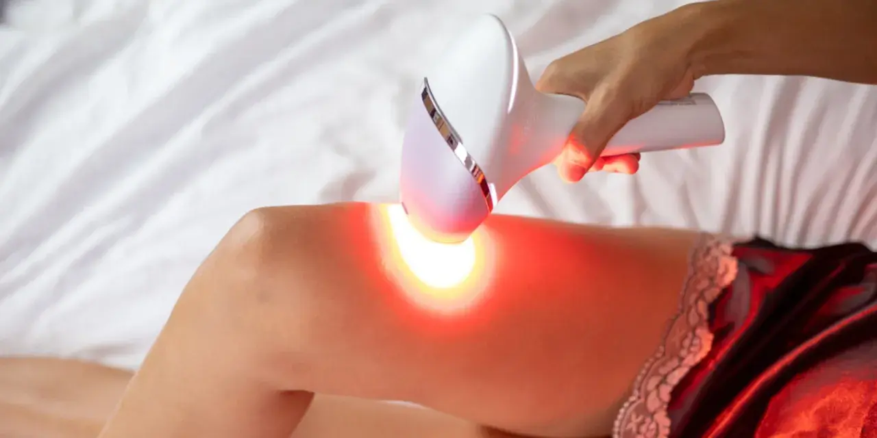 Dłoń trzyma depilator laserowy nad udem, emitując czerwone światło. Czy depilacja laserowa jest szkodliwa?