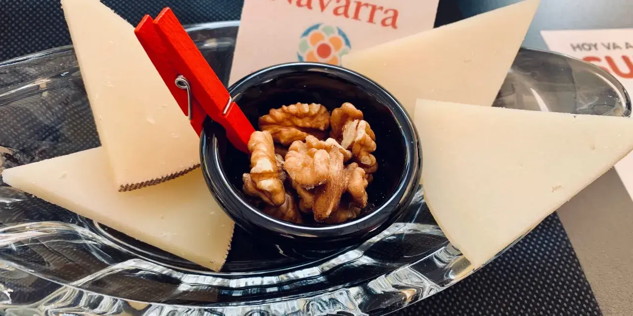 Queso en cuñas con nueces en un cuenco negro, sobre plato de cristal y tarjeta "Reino de Navarra".