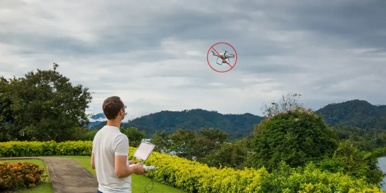 Man with drone controller looks at a drone with a "no fly" symbol, illustrating ct drone laws.