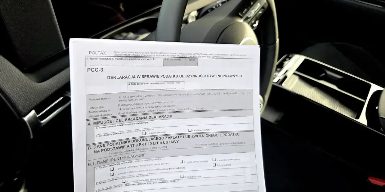 Deklaracja PCC-3, dokument dotyczący podatku od kupna samochodu, leży na desce rozdzielczej auta.