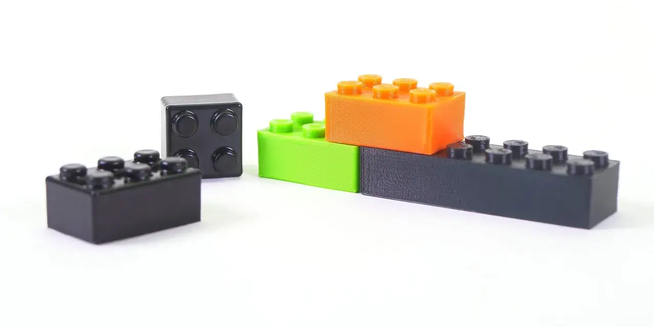 Klocki z drukarki 3D, wykonane z materiału ABS, w kolorach czarnym, zielonym i pomarańczowym, ułożone na białym tle.