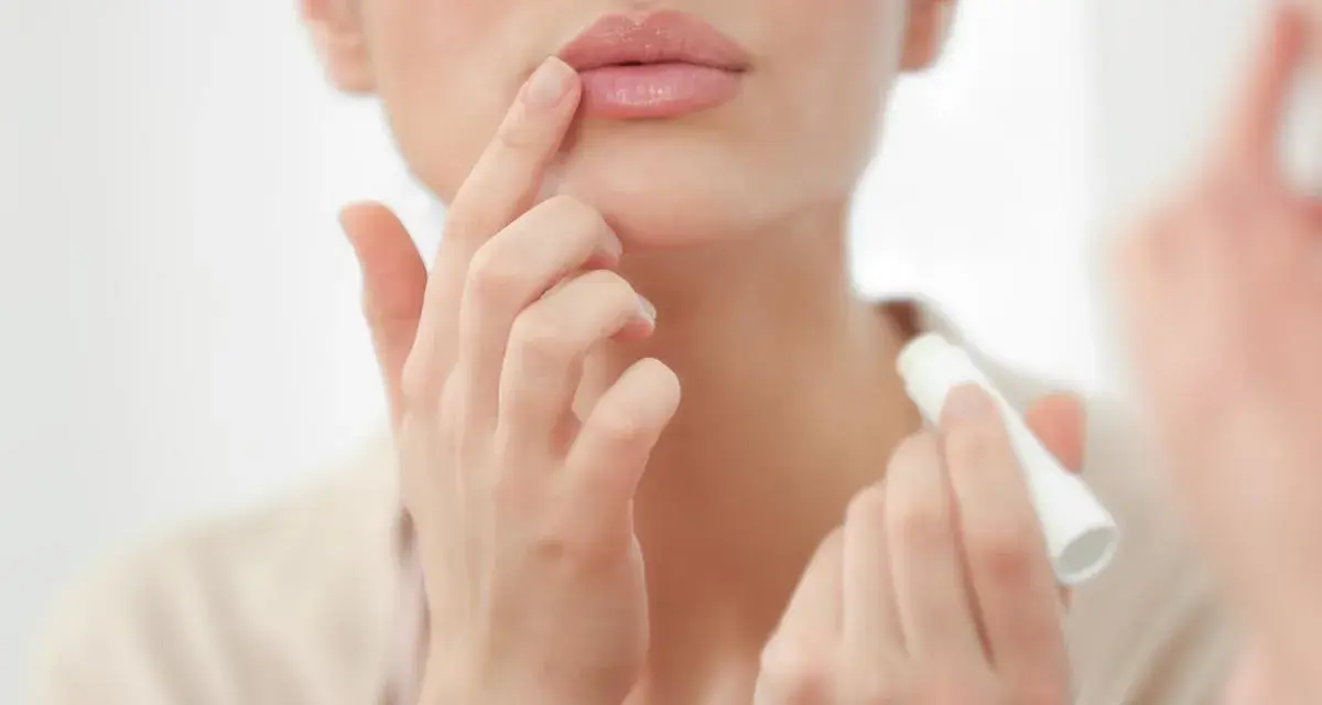 Una mujer aplica bálsamo labial, mostrando cómo son los labios perfectos: hidratados y suaves.