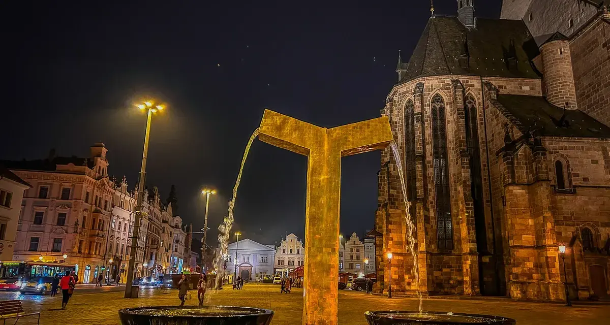 Złota fontanna w centrum miasta, obok zabytkowego kościoła. Wieczorne Pilzno, pełne urokliwych atrakcji.