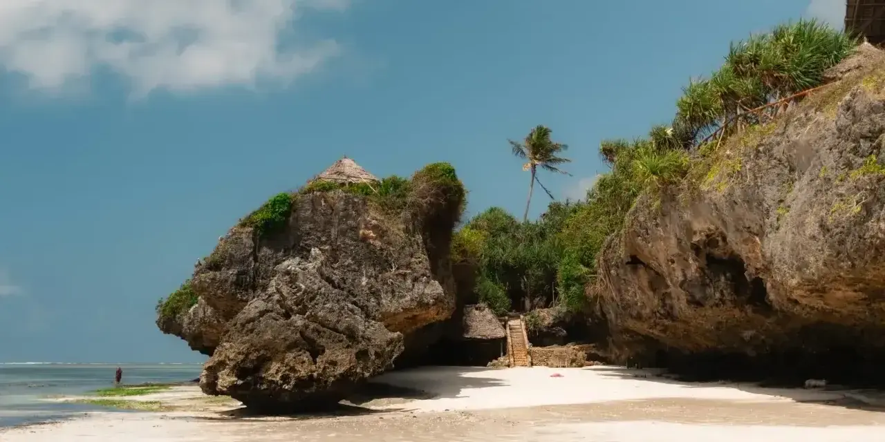 Piękna plaża na Zanzibarze w kwietniu. Skaliste klify, palmy i chatki z trawy tworzą rajski krajobraz.