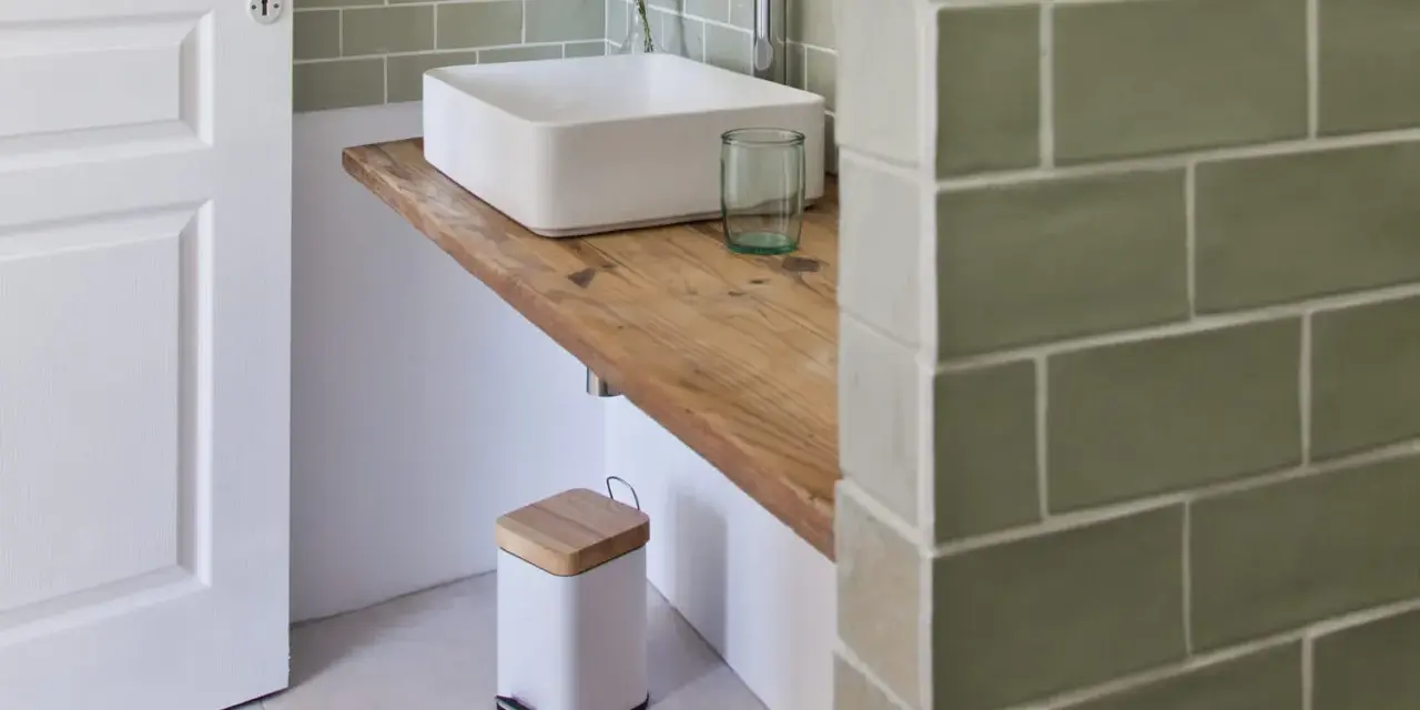 Plan de travail pour salle de bain avec lavabo carré, robinetterie moderne et poubelle design.